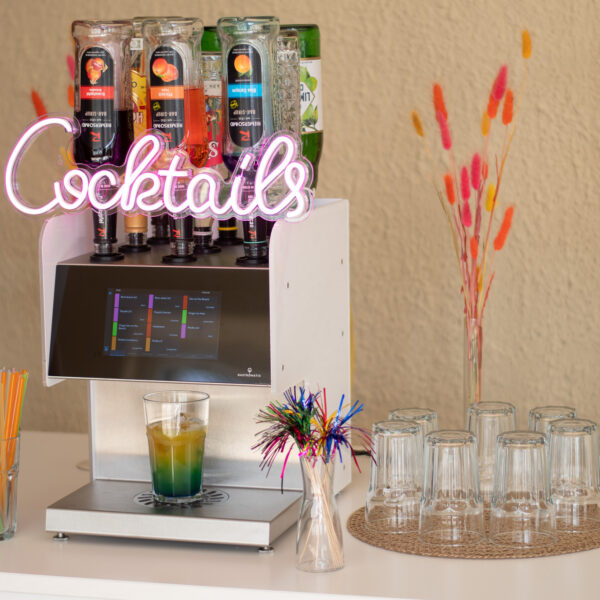 Eine Cocktailmaschine aufgebaut auf einem Tisch mit Gläsern, Strohhalmen und Dekoration